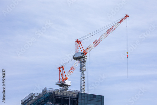 two large red and white cranes on the top of a skyscraper against a blue sky