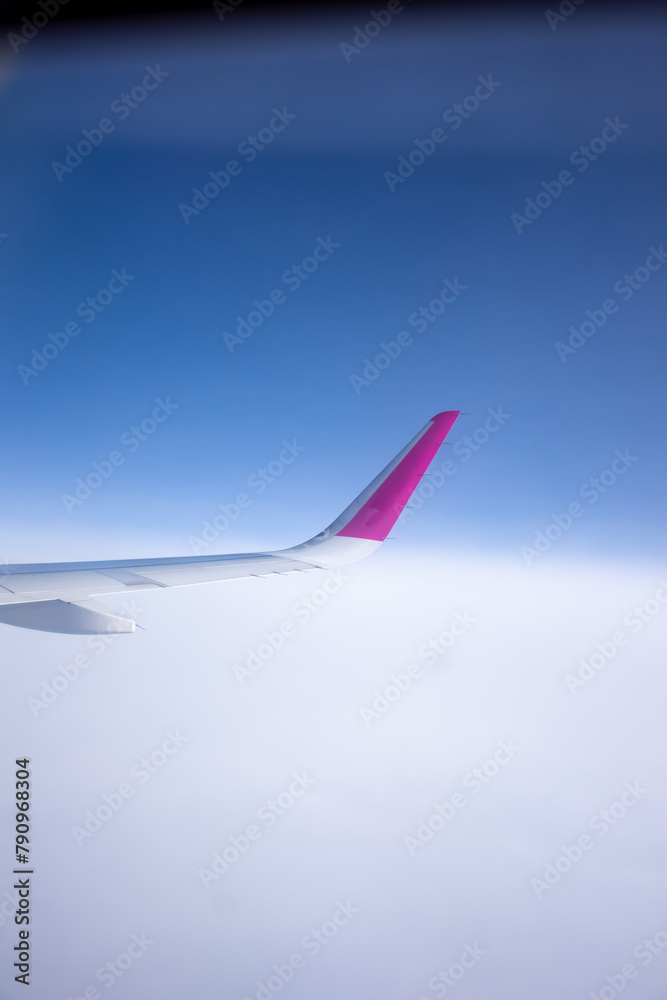 Fototapeta premium A pink and white aircraft wing soars through the cloudy sky
