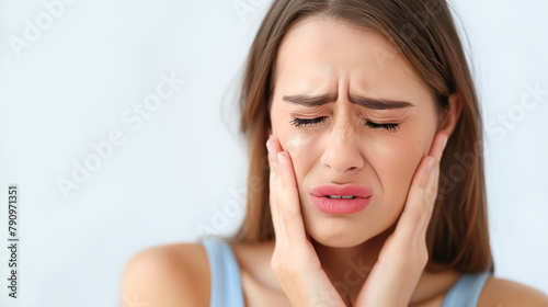 Young woman holds her cheek with her hand and suffers from severe toothache, light background. Dental diseases concept, problems with teeth and tooth enamel