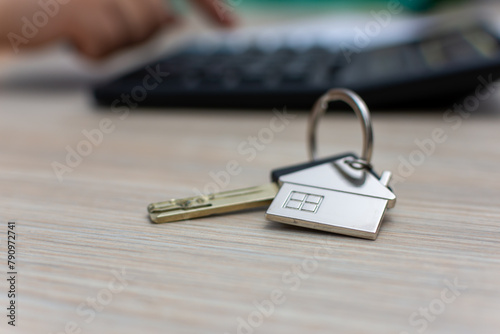 Metal keys with house keychain on wood table near calculator