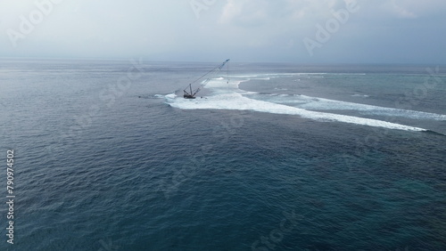 Aerial view of waves crashing on a sunken barge with a crane