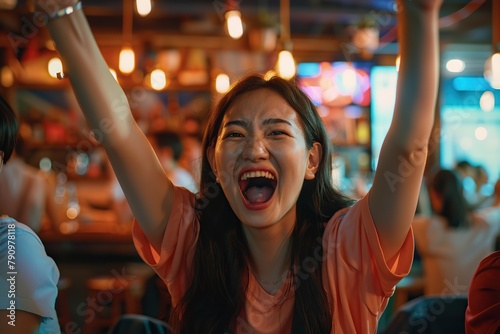 Two young asian women sitting at cafe watching TV football  drinking beer  raising hands up. Girls shouting feels overjoyed happy by favourite soccer club team winning get victory  sports betting.