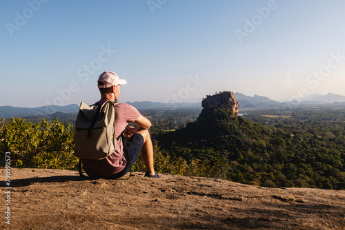 Man with backpack sitting on rock and looking at landscape. Beautiful scenery with Sigiriya rock. Solo traveler in Sri Lanka. . © Chalabala