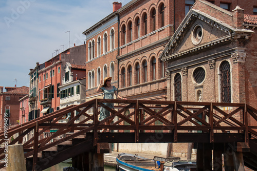 Tourist woman standing on empty bridge with panoramic view of water channel in city Venice, Veneto, Italy, Europe. Venetian architectural landmarks and old houses facades along water traffic corridors