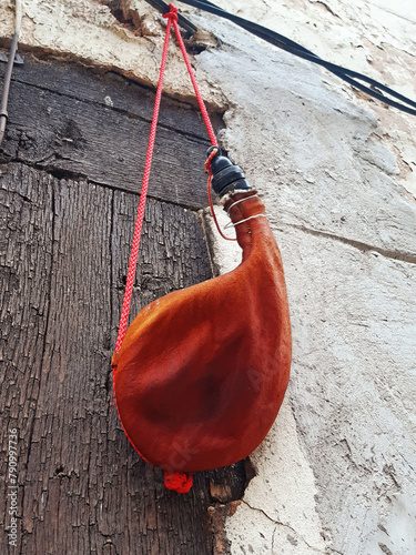 Wineskin. Red Wine leather bottle hanging. Closeup of handmade curved wine boot. Leather goods and traditional crafts.