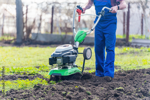A farmer in the garden tills the land with a motorized cultivator or power tiller, preparing the soil for planting crops photo