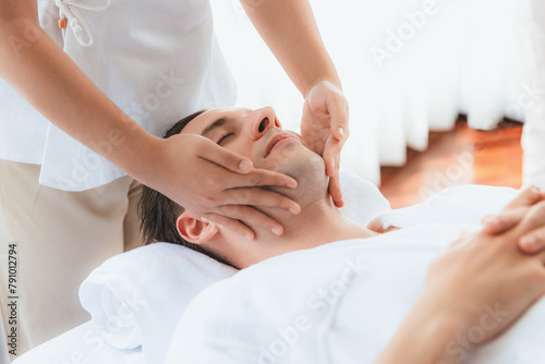 Caucasian man enjoying relaxing anti-stress head massage and pampering facial beauty skin recreation leisure in dayspa modern light ambient at luxury resort or hotel spa salon. Quiescent