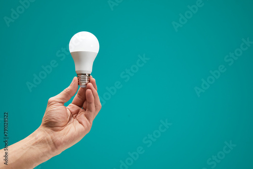 Hand holding a LED light bulb isolation on green background. Male hand demonstrating Eco power light bulb. Innovation inspiration concept.
