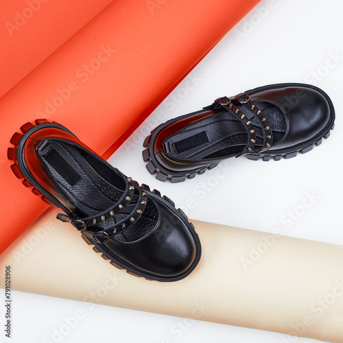 Pair of black boots with thick or massive soles. Modern female black shoes on orange and beige background. Long paper tube or paper roll and fashion leather shoes.
