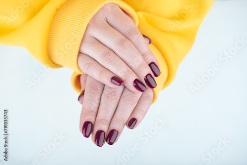 Women's hands in yellow sweatshirt with stylish blackberry color manicure on nails.
