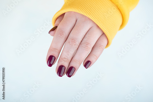 Woman's hand over light background with stylish blackberry color manicure on nails.