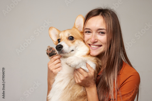 a brunette girl holds and hugs a red corgi dog on a clean light background, the concept of love for animals