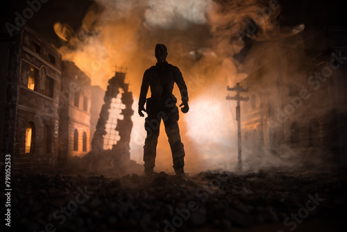 Artwork decoration. A man standing on a road of burnt up city. Apocalyptic view of city downtown as disaster film poster concept. Night scene. City destroyed by war. © zef art