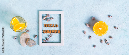 Hello summer text in photo frame, cocktail, orange, stones and seashells on blue top view web banner