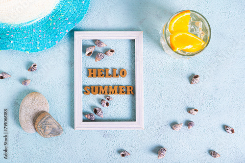 Hello summer text in photo frame, cocktail, hat, seashells and stones on blue top view