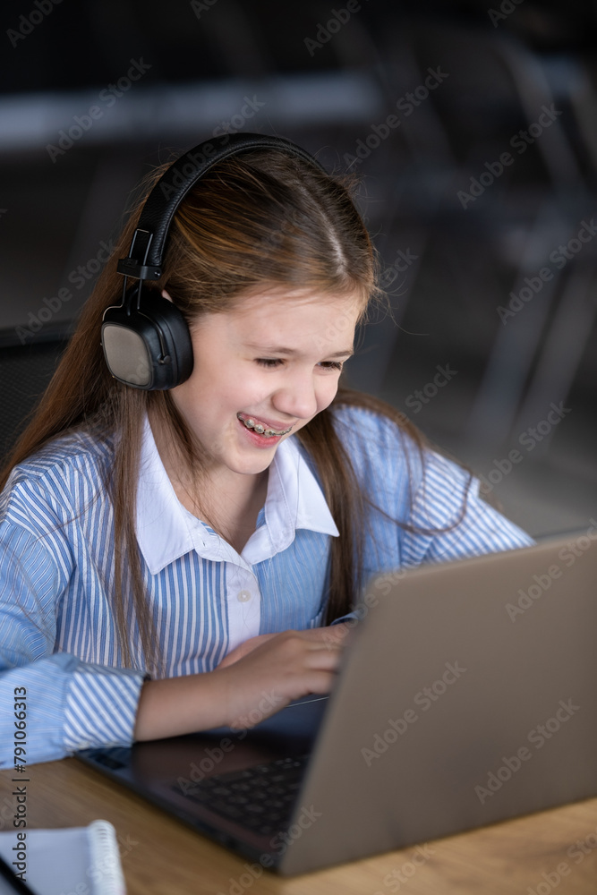 A laughing girl in braces sits at a table in front of a laptop. A laughing girl in braces sits at a table in front of a laptop.