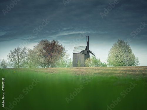 view to old wooden mill between green field and dark clouds