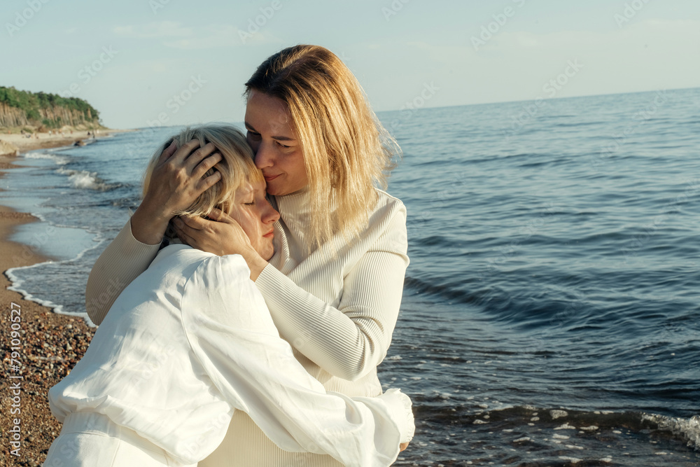 Mom hugs her daughter on the beach by the sea.