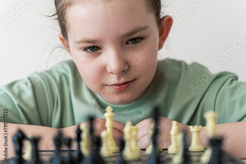 Cute little girl playing chess and looking with concentrated eyes at chessboard. Selected focus. photo