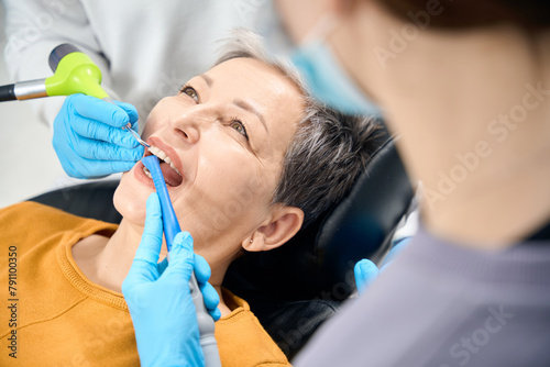 Nurse holds saliva ejector while dentist engaging in professional tooth cleaning