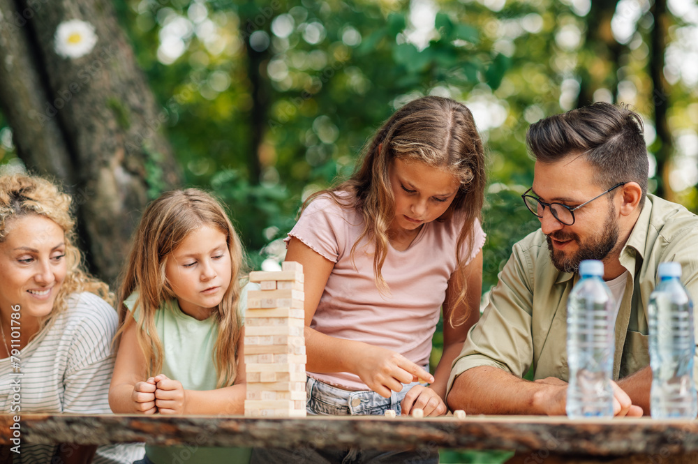 Girl is rolling dices and playing jenga with her family in nature.