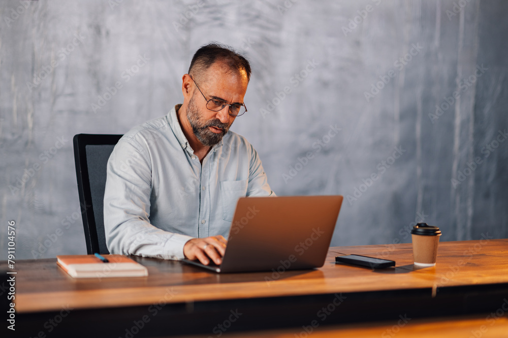 Mature businessman typing on a laptop at modern corporate office. Mature businessman typing on a laptop at modern corporate office.