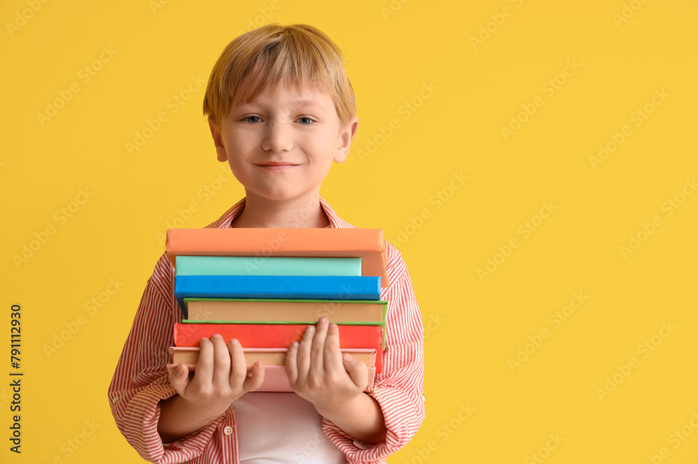Cute little boy with stack of books against yellow wall Cute little boy with stack of books against yellow wall
