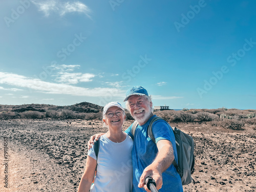Outdoor activity in nature concept. Carefree smiling sporty senior couple take selfie walking in Tenerife Punta Rasca reserve enjoying healthy lifestyle and freedom in good sunny day with blue sky © luciano