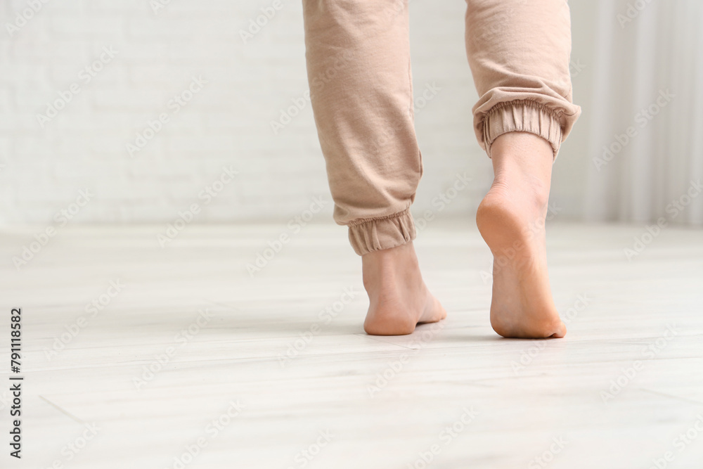 Barefoot woman walking on laminate floor in room, back view