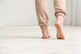 Barefoot woman walking on laminate floor in room, back view