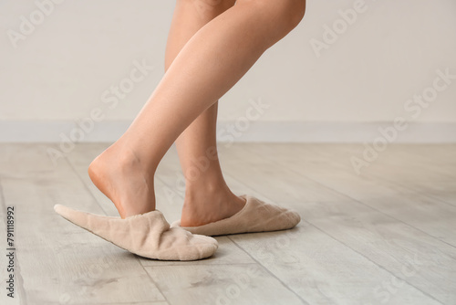 Woman in soft slippers walking on laminate floor near light wall, closeup