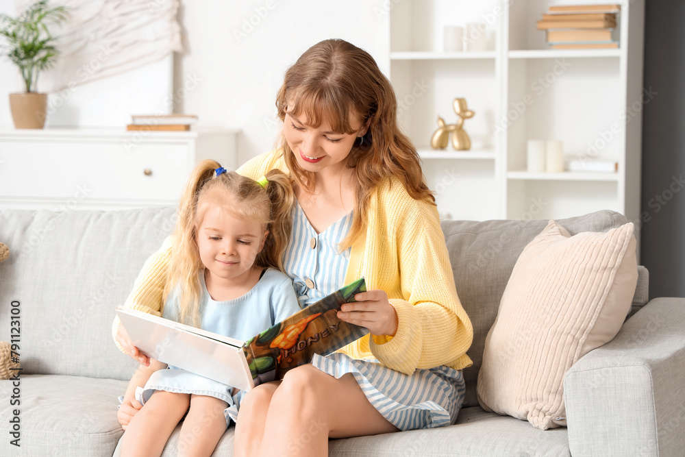 Fototapeta premium Nanny reading story to little girl on sofa at home