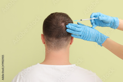 Young man with hair loss problem receiving injection on green background, back view