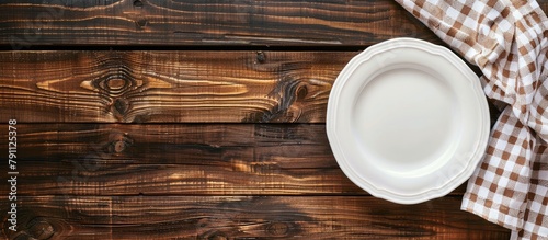 Wooden table background with an empty plate and towel  seen from above  providing space for text.