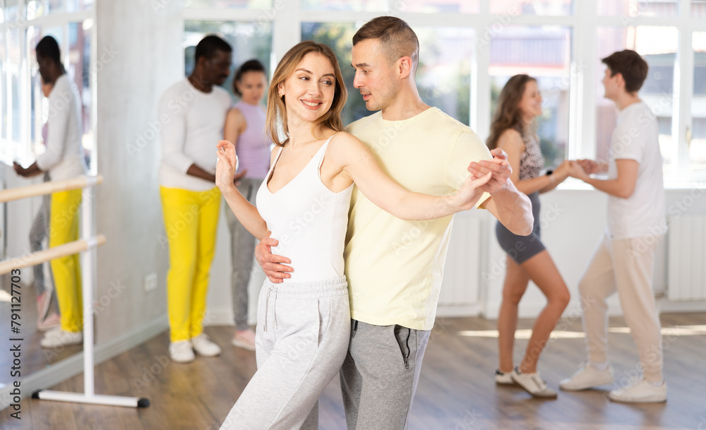Fototapeta premium Positive woman and man dancing bachata in pair during group dance classin dancing studio
