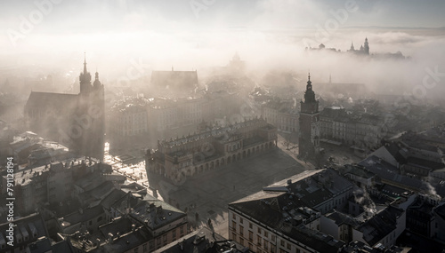 Soft lighted Main Square in Krakow (view of Saint Mary Basilica - Mariacki Church, cloth hall - Sukiennice, town hall and Wawel castle) during beautiful, foggy sunrise, Poland photo