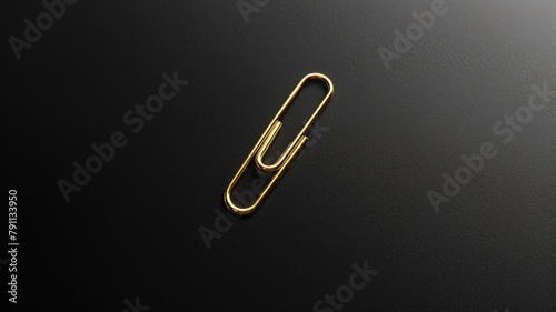 Single gold paperclip on black surface photo