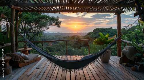 Fototapeta Naklejka Na Ścianę i Meble -  A hammock hangs on a wooden porch overlooking a jungle canopy at sunset.