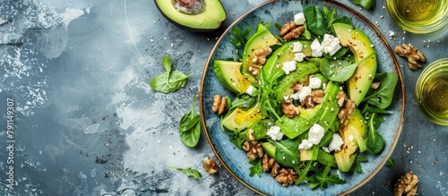 Vibrant midday meal - a salad with springtime flair. Crisp greens combined with avocado, walnuts, feta cheese, and olive oil, presented in a sky blue dish. photo