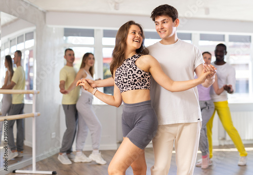 Slim young man and woman practicing salsa dance in training hall during group dancing classes photo