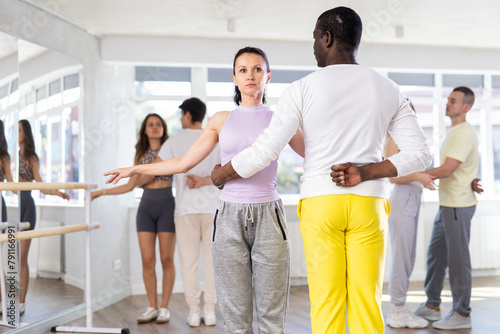 Positive middle-aged woman and Afro-American man engaged in waltz dance in dancehall during workout session