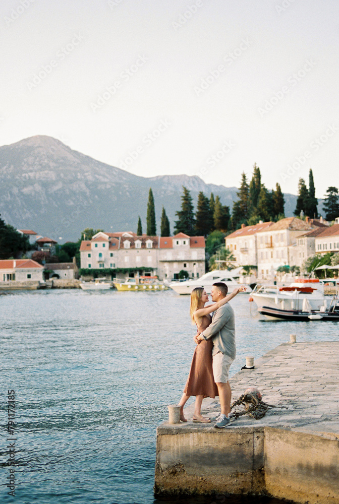 Man and woman stand hugging and almost kissing on the pier of the ancient village of Rose. Lustica, Montenegro