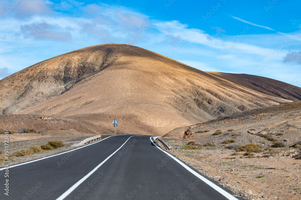 Fototapeta premium Mountain road on colourful remote basal hills and mountains of Massif of Betancuria, Fuerteventura, Canary islands, Spain