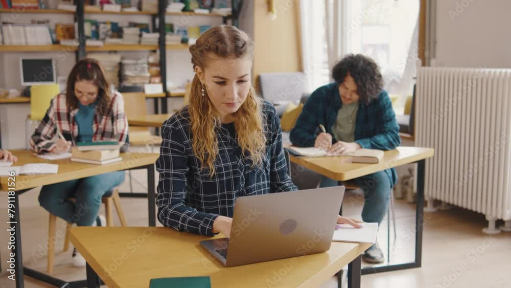 a group of students study and read books, write information in notebooks, on their phones and laptop in a library or classroom. Students in a good mood studying and reading books in the library