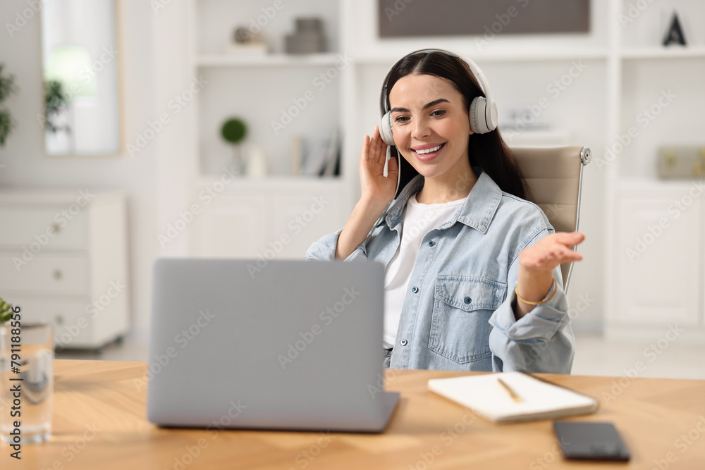 Young woman in headphones using video chat during webinar at table in room Young woman in headphones using video chat during webinar at table in room
