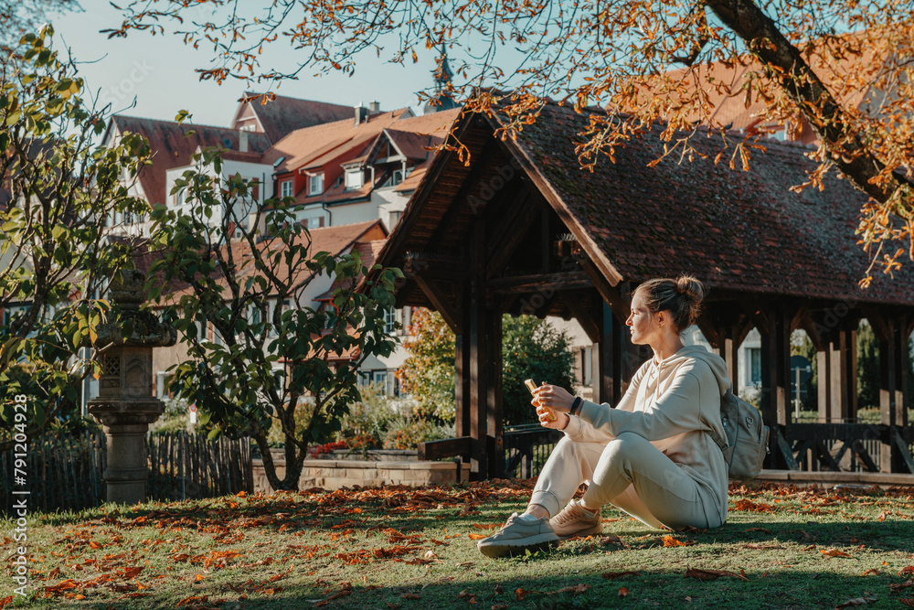 Obraz premium Young Fashionable Teenage Girl With Smartphone In Europian Park In Autumn Sitting At Smiling. Trendy Young Woman In Fall In Park Texting. Retouched, Vibrant Colors. Beautiful Blonde Teenage Girl