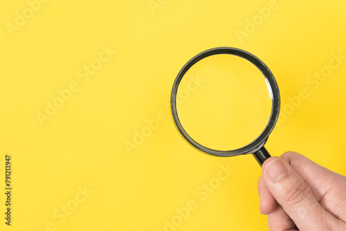 Man hand holding a classic magnifying glass isolated on yellow background