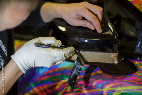 A specialist in wrapping a car vinyl film in the process of work. Car wrapping specialists cover the car with vinyl sheet or film close-up. Selective focus.