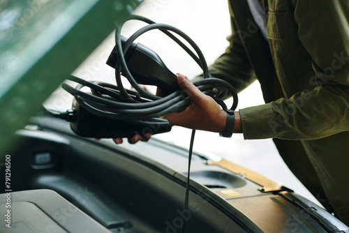 Closeup image of electric car driver putting charging cable in trunk