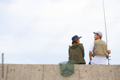 釣りをしながら堤防に座って話す男女 photo